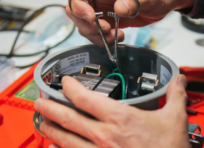 A close-up of a Utilidata smart meter, with a pair of hands holding a tool.