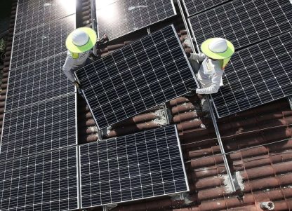Two people works on a solar panel project on the roof of a home.
